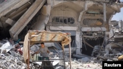 ایک فلسطینی شخص اسرائیلی حملے میں تباہ شدہ گھروں کے قریب ایک عارضی دکان پر کھڑا ہے۔ 