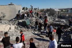 مغربی کنارے میں اسرائیل کے زیر قبضہ علاقے میں لوگ ایک فلسطینی عسکریت پسند یحییٰ ماری کے گھر کے باہر کھڑے ہیں جسے اسرائیلی فورسز نے دھماکے سے اڑا دیا تھا۔ 26 فروری 2023