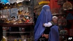بچے کے ہمراہ برقعے میں ملبوس ایک خاتون کابل کی ایک مارکیٹ سے گزر رہی ہے۔ آٹھ مئی 2022ء