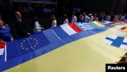یورپئین قانون ساز اور یوکرین کے نمائندے برسلز میں پورپی پارلیمنٹ کے باہر یوکرین کا پرچم لیے کھڑے ہیں (رائٹرز)
