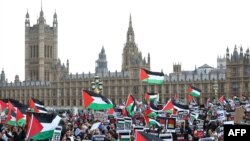 Người biểu tình cầm biểu ngữ và vẫy cờ Palestine khi họ đi bộ qua Cầu Westminster, đằng sau là Điện Westminster, trụ sở Nghị viện Anh, trong cuộc 'Tuần hành vì Palestine' ở London, Vương quốc Anh, ngày 28 tháng 10 năm 2023, để kêu gọi hưu chiến giữa Israel và Hamas.