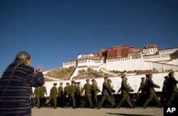 Một người phụ nữ Tây Tạng cầu nguyện trong lúc một nhóm binh lính Trung Quốc diễu hành ở phía trước Cung điện Potala ở Lhasa.