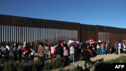 امریکہ اور میکسیکو کی سرحد پر نصب آہنی دیوار کے نزدیک تارکین وطن جمع ہیں۔ (فائل فوٹو)