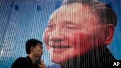 Một người đi ngang qua tấm áp phích có ảnh Đặng Tiểu Bình, một lãnh đạo của Đảng Cộng sản Trung Quốc trước đây. Các chuyên gia cho rằng sự phát triển kinh tế của Trung Quốc bị chậm lại là do vấn đề trong nước hơn là do thương chiến với Mỹ.
