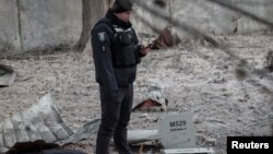 Một cảnh sát đứng gần các bộ phận của máy bay không người lái tại địa điểm tòa nhà bị phá hủy bởi cuộc tấn công của Nga vào ngày 14/12/2022. Trên máy bay có dòng chữ "Dành cho Ryazan!!!"