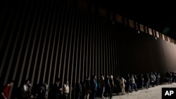 Di dân sắp hàng dọc bức tường biên giới chờ đệ đơn xin tị nạn sau khi từ Mexico vượt biên sang Mỹ, ngày 11/7/2023, gần Yuma, Arizona.