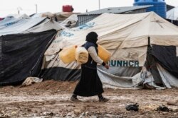 کردوں کے زیر انتظام الہول کیمپ میں ایک خاتون پانی لینے جا رہی ہے۔ اس کیمپ میں داعش کے جنگجوؤں کے خاندانوں کو رکھا گیا ہے۔ دسمبر 2019